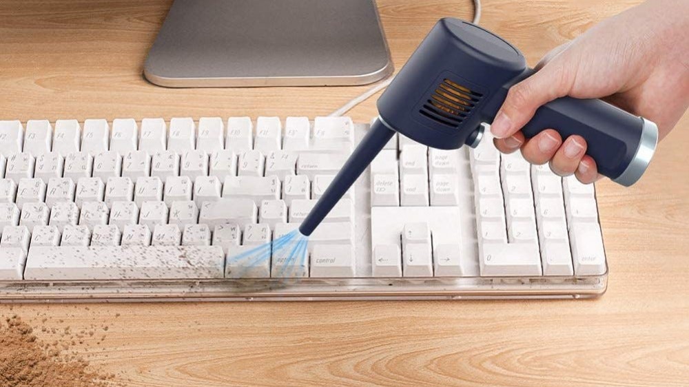 Electric air duster being used to clean dust from a keyboard.